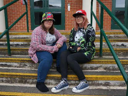 two young women sat together wearing brightly coloured hats