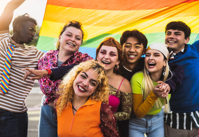 group of seven teenager or mixed genders at a festival holding up a pride flag