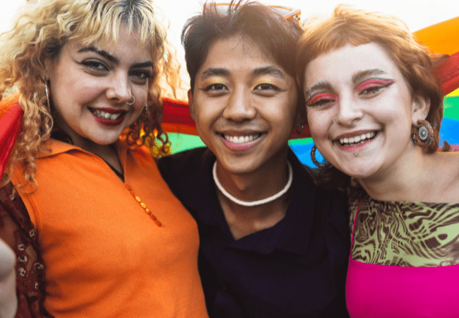 Group of three teenagers smiling with pride flag draped round them
