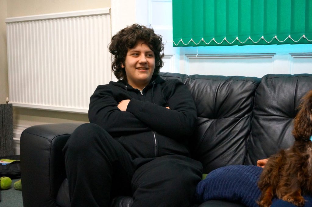 young man sat on sofa, arms folded leaning back and smiling